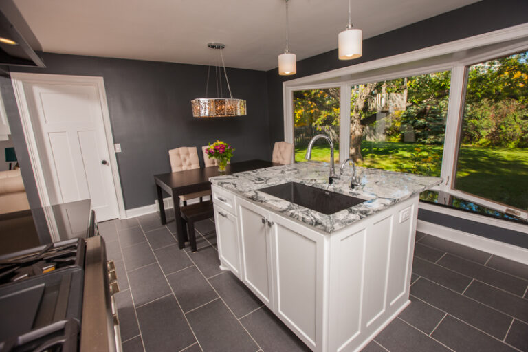 Residential kitchen with cabinet painting in crisp white, gray marble island, dark tile floors, and charcoal walls in Sain...