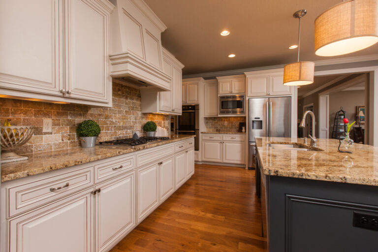 Residential kitchen cabinet painting in crisp white with glaze finish, granite countertops, brick backsplash, and hardwood...