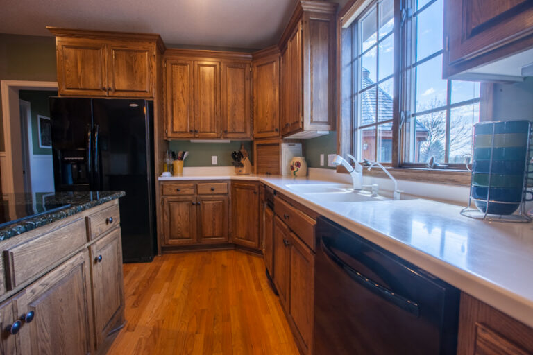 Oak wood kitchen cabinets and green walls in a home kitchen, ready for a DIY painting project.