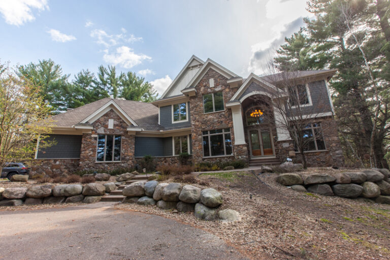 Freshly painted grey siding and white trim on a large stone house set in a wooded landscape.