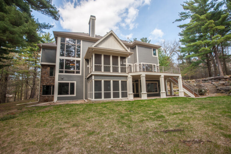 Freshly painted gray siding and white trim on a multi-story house in a wooded backyard setting.