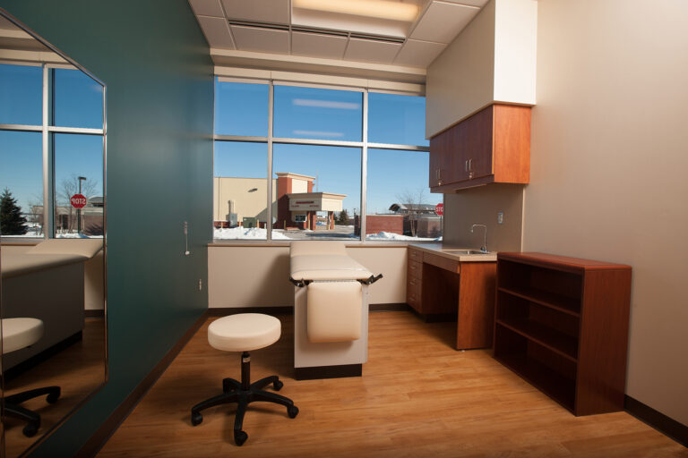 Teal accent wall painted in a bright medical examination room with wood cabinetry and a window.