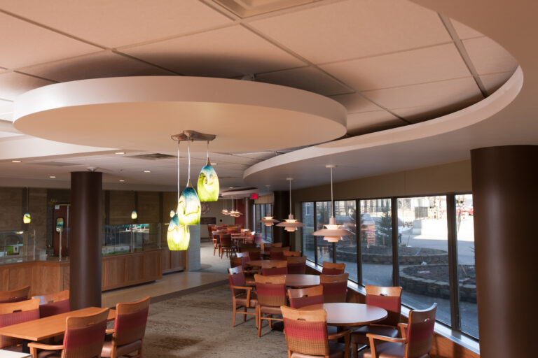 Interior painting of a commercial dining space with warm tan walls, decorative ceiling, and colorful pendant lights in Sai...