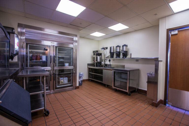 Commercial kitchen interior painting with crisp white walls, stainless steel equipment, and terracotta tile floors in Sain...