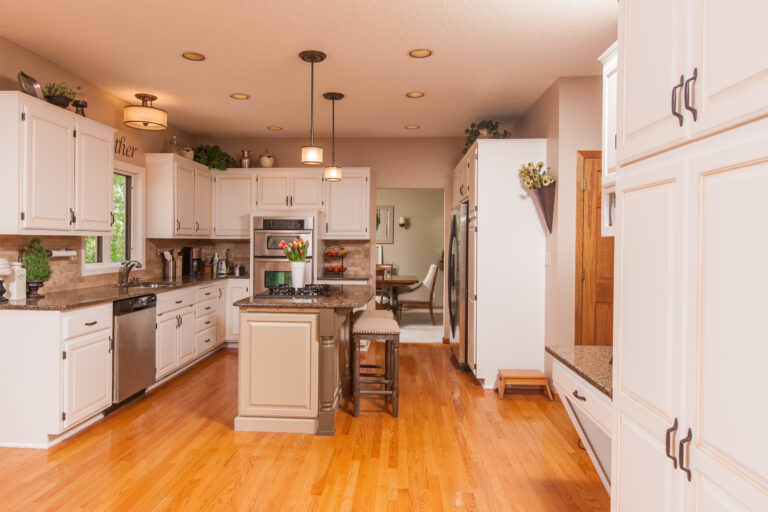 Freshly painted white wooden kitchen cabinets and island in a home with hardwood flooring.