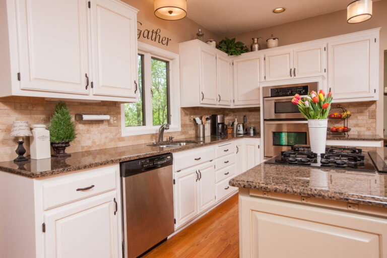 Freshly painted white wood cabinets in a kitchen with granite countertops and stainless steel appliances.