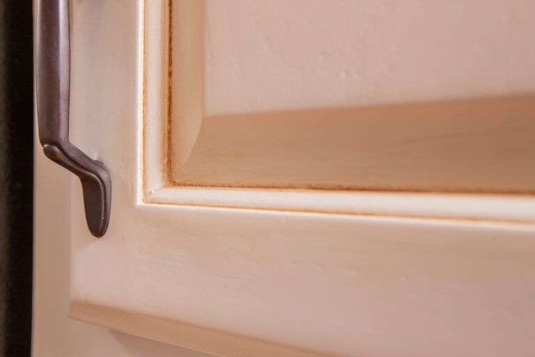 Close-up of a white painted wood kitchen cabinet door with brown glaze in the recessed trim.