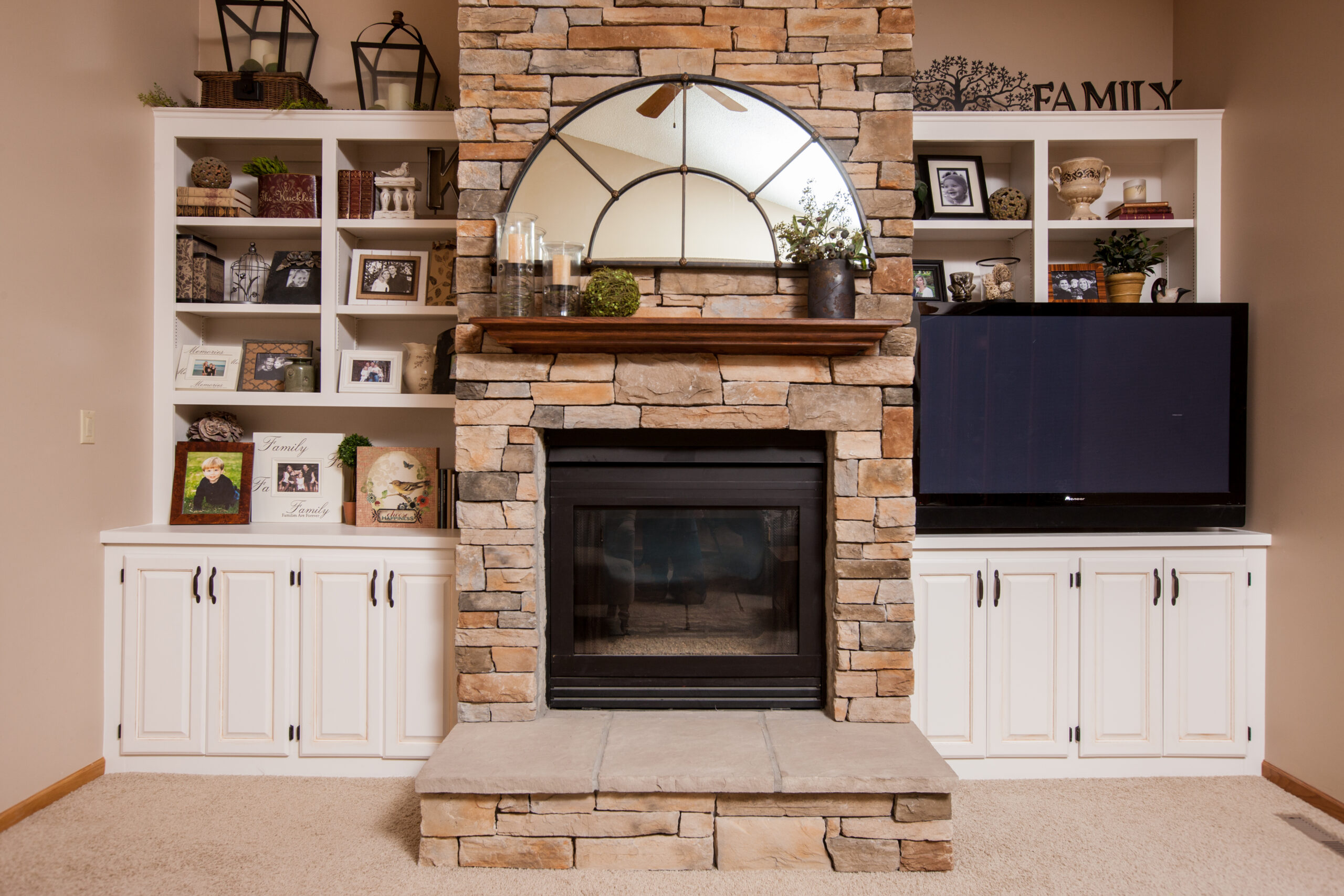 White painted built-in cabinets and shelving flanking a stacked stone fireplace in a living room.