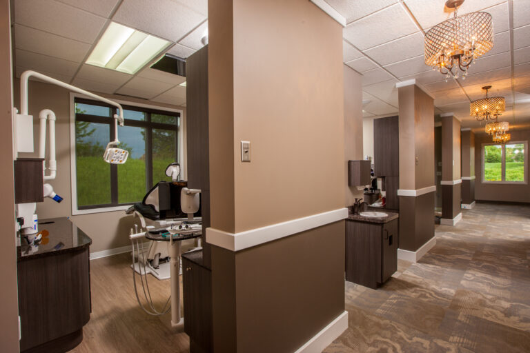 Interior painting of a modern dental office hallway with warm taupe walls, white trim, and elegant chandelier lighting in ...
