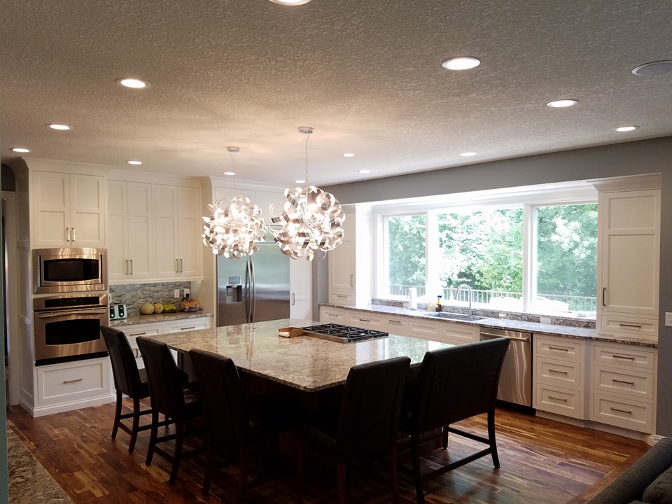 Newly painted white cabinets in a modern kitchen with a large granite island and stainless steel appliances. Painted interior walls in St. Paul Mn.