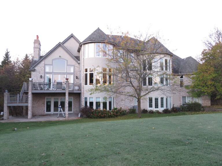 Exterior painting project on a large multi-story house with brick and stucco siding in a grassy backyard.