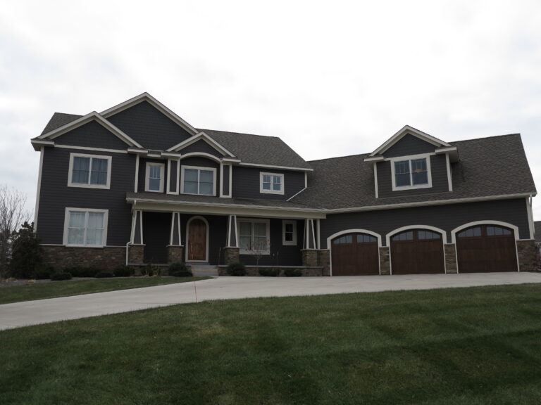 Freshly painted dark gray siding and white trim on a large two-story house with a three-car garage.