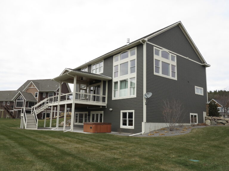 Exterior painting on a two-story residential home with dark gray siding, white trim, and an elevated deck in Minnesota.
