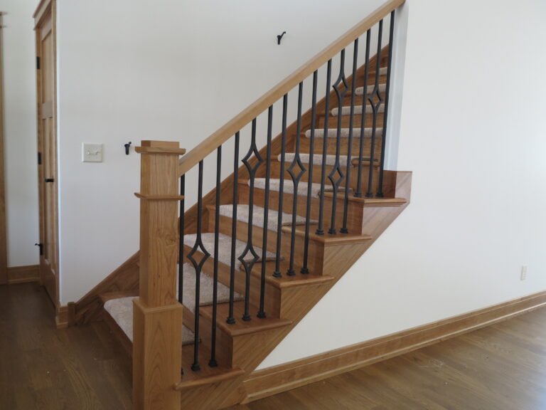 Interior wooden staircase with black metal balusters and a wood newel post in a home with white painted walls in Minneapolis MN.