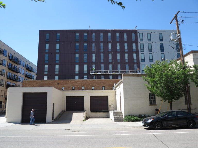 Workers on a suspended scaffold doing exterior painting on a dark brown multi-story commercial apartment building in Saint...