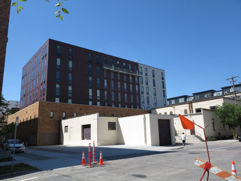 Exterior painting on a large multi-story mixed-use building with dark brown panels and white lower facade in Saint Paul.