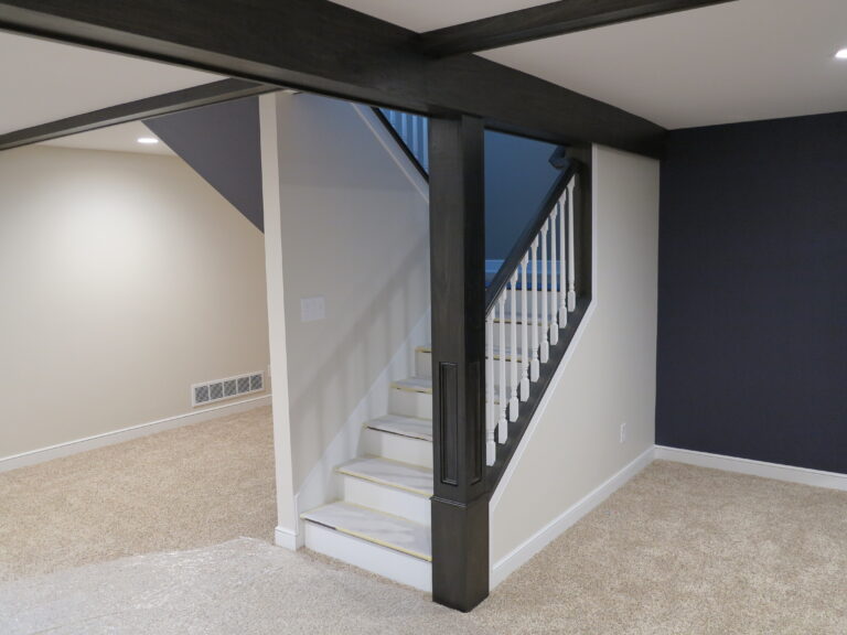 Freshly painted basement featuring dark stained wood beams, white trim, and neutral walls.
