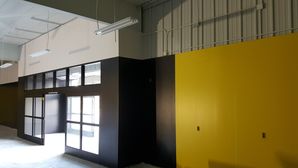 Interior painting of a commercial building featuring bold yellow and black walls with industrial windows and high ceilings.