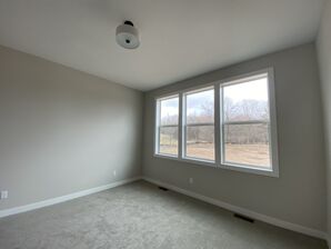 Freshly painted gray walls and white trim in an empty room with large windows and gray carpet.