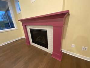 Wooden fireplace mantel painted deep pink in a living room with yellow walls and light wood floors. Minneapolis MN.