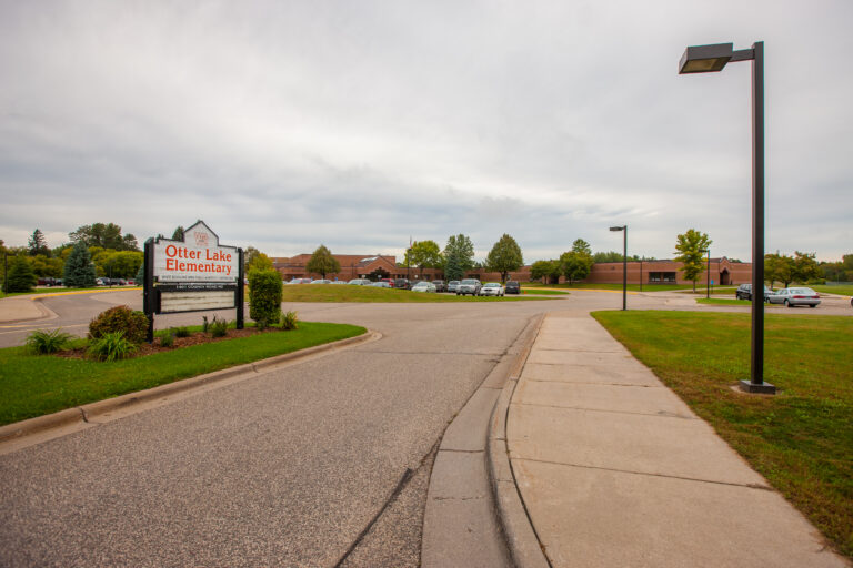 Exterior of Otter Lake Elementary school featuring brick building surfaces, metal light poles, and a paved parking lot.