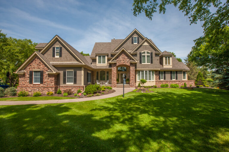 Exterior painting on a large two-story brick and cedar shake residential home with lush green lawn in Saint Paul, MN