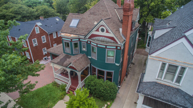 Aerial view of a Victorian home exterior painting project in deep green with red trim and decorative gables, Saint Paul, MN