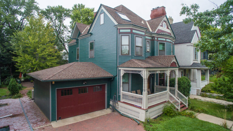 Freshly painted teal house with white trim and a red garage door in a residential neighborhood.