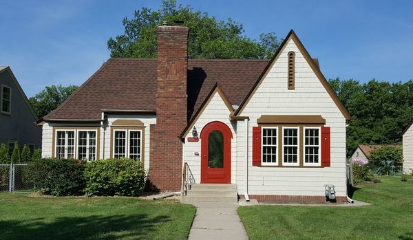 Freshly painted white shingle house with red door and brown trim in a residential yard.
