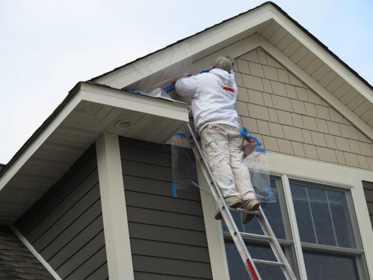 A painter on a ladder doing exterior painting on a two-story residential home's upper gable trim in Saint Paul, MN.